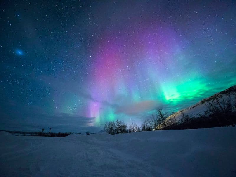 Green and purple northern lights over snowy mountains