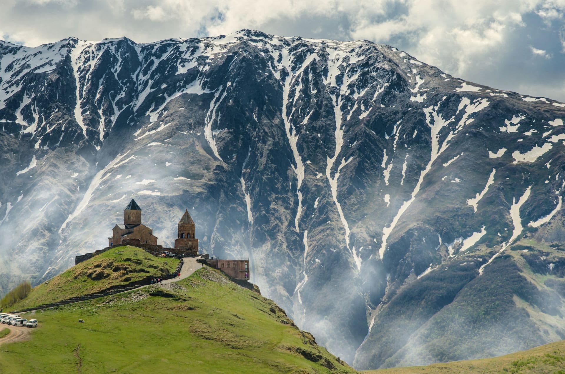 Gergeti Trinity Church on a green hilltop below a snow-streaked mountain in Kazbegi