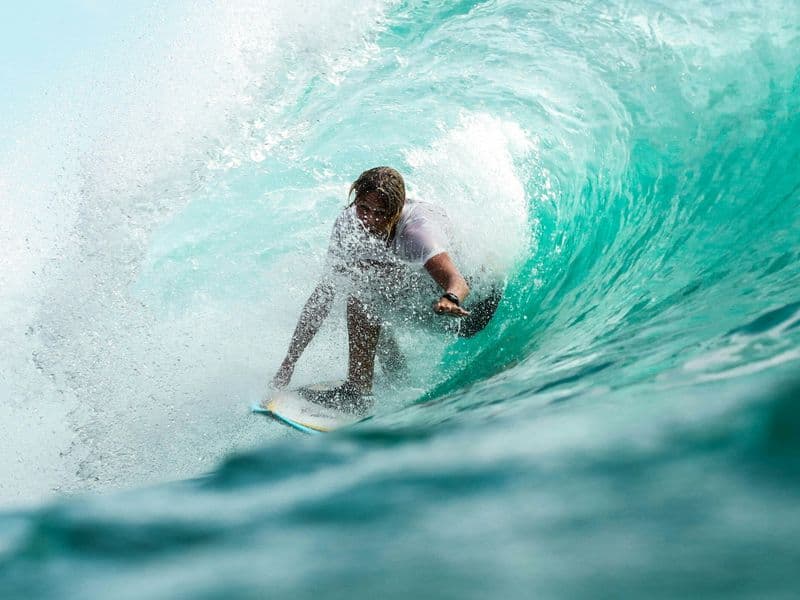 A surfer riding inside a curling turquoise wave