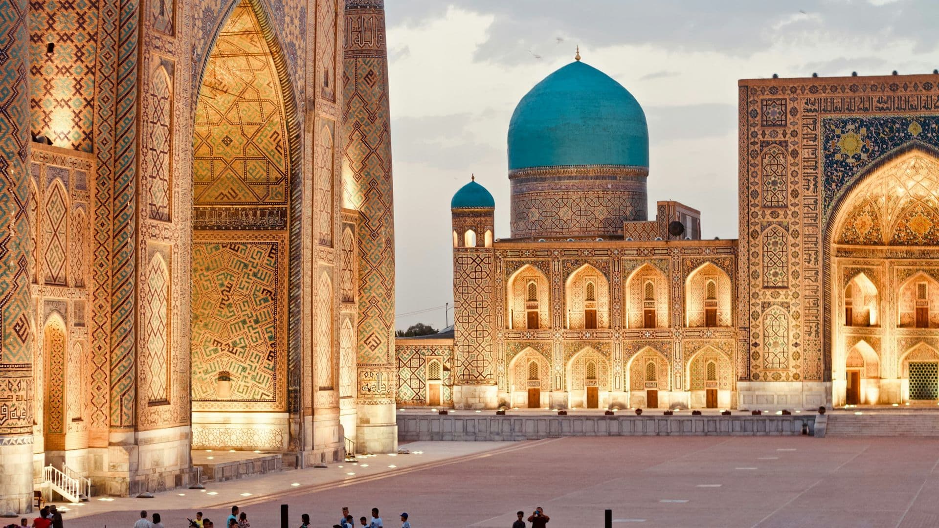The tiled madrasas and turquoise dome of the Registan in Samarkand, lit up at dusk