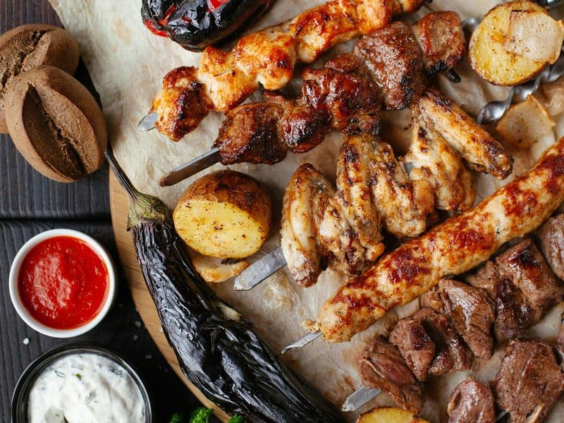 Grilled meat, potatoes and dipping sauces on a wooden board