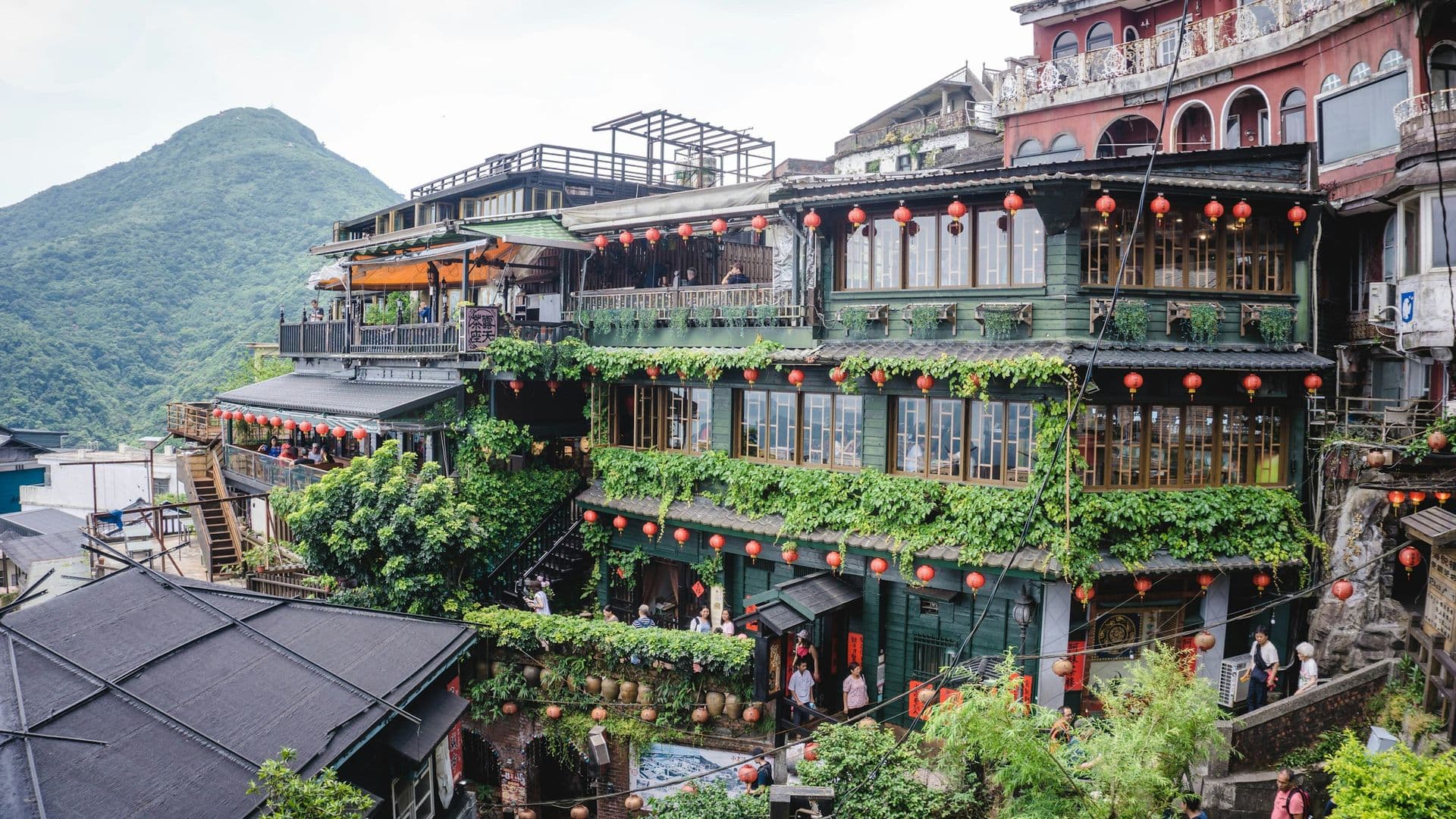A wooden teahouse hung with red lanterns on a green hillside in Jiufen